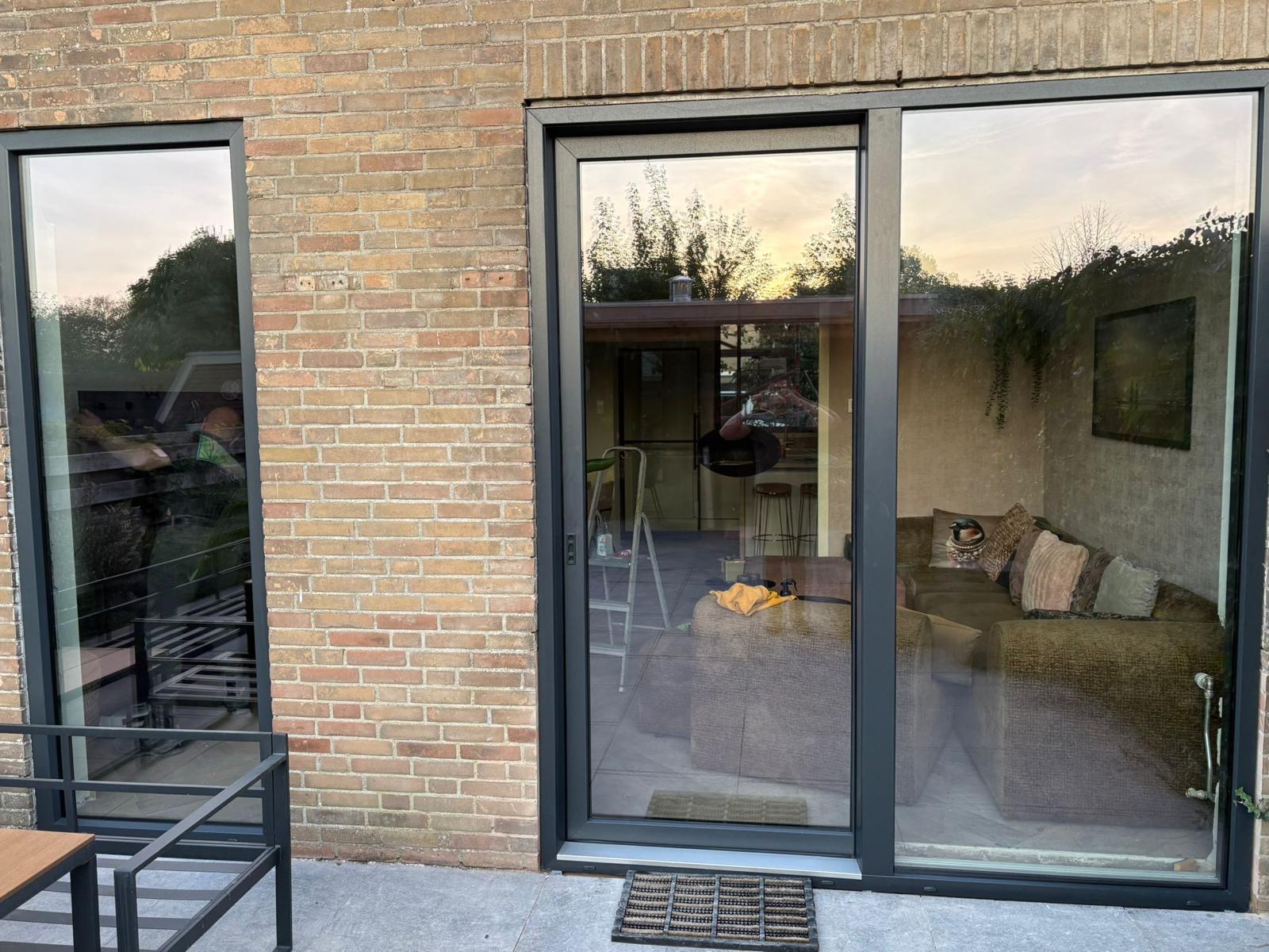 Antraciet terrasdeur met kruk en vast glasdeel, links een smal raam achter een bakstenen penant